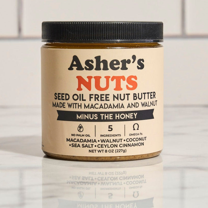 Jar of Asher's Nuts seed oil free nut butter on a marble surface with a tiled wall background